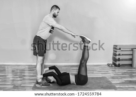 Young couple practicing yoga together. Indoor picture of handsome tanned guy on mat doing standing pose s to strengthen legs, stretching arms and looking up with blonde woman.