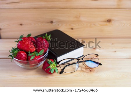 Bible, glasses, red strawberries in a vase on a wooden background. Warm tone. There is a place for the inscription. Good morning.