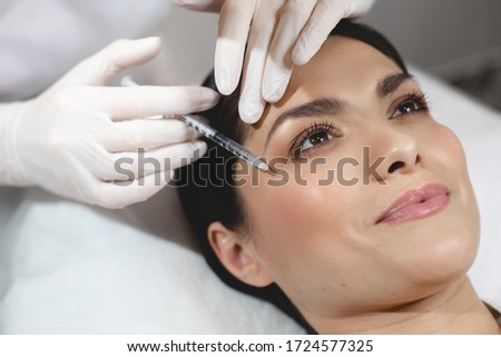 Injection process under facial skin at eye area with syringe. Young happy woman lying during procedure. Beautician does it carefully Royalty-Free Stock Photo #1724577325