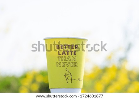 coffee take-away in a yellow paper cup, without text. standing against a yellow flower filed, place for copy.