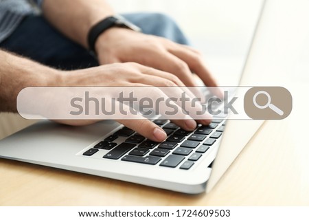 Search bar of internet browser and man working on modern laptop at table indoors, closeup