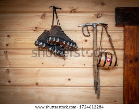 Vintage climbing leather boots and ice ax hang on a wooden wall. Antique Climbing Equipment