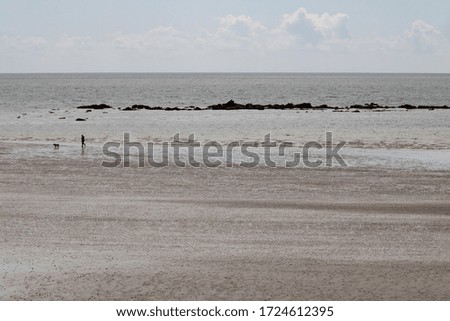 A stunning, peaceful view of an empty beach off season with a tiny silhouette of a sole person walking their dog in the distance, Cornwall, United Kingdom.