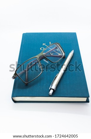 closed spiral notebook with pen and eyeglasses on isolated white background.