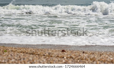 Foamy white waves on sea water surface with green and turquoise colors, blurred bokeh effect of wet beige sand on the beach coast, shallow depth. Natural colorful pattern, suitable for backgrounds.