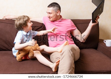 Funny young father sit on computer laptop fool around with cute kid son have fun together, smiling dad and little boy child enjoy stay at home rest on couch with gadgets. Online education and work.