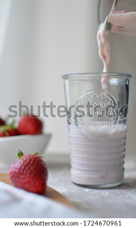 Strawberry smoothie with milk. Vase with strawberries. Pourin from a mixer into a glass beaker. Image this selective focus