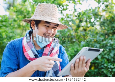 Thai gardeners wear a mask to protect against the virus Kovid-19 Intentionally reading news on the tablet screen in the garden, the concept of follow-up on coronavirus-19 and the economy