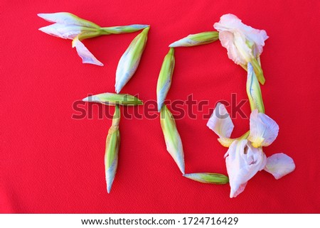 Number 70 written by fresh iris flowers on a red background. Number seventy written in fresh flowers isolated on red. 