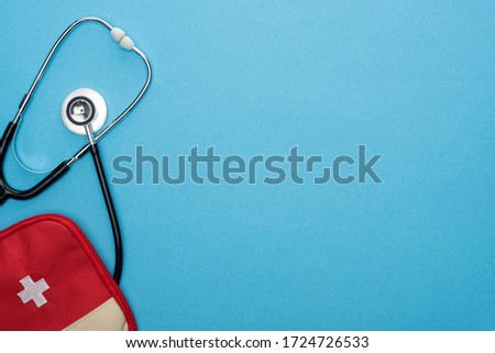 top view of red first aid kit and stethoscope on blue background