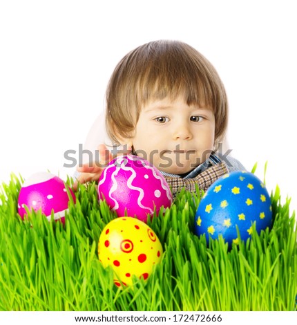 Cute Baby boy hunting for colorful Easter Eggs, hidden in the green grass, close up face portrait. Studio shot, over white background, isolated, with copy space. 