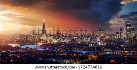 Elevated, panoramic view to the lit skyline of London, United Kingdom, during sunset time with colorful clouds and rain