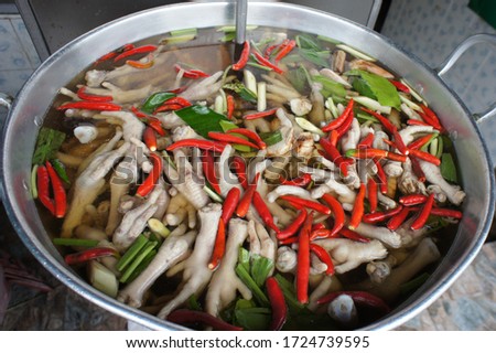 Picture from above of chicken Feet Spicy Soup in a large metal pot. In the pot there are chicken feet, lemongrass, kaffir lime leaves, celery, chilli, galangal and soup.