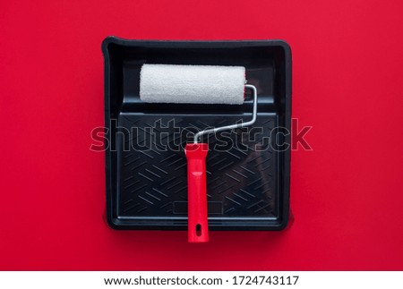 Paint roller, black tray on a red background. View from above. Concept
