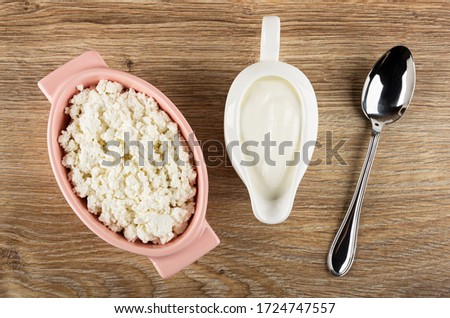 Pink glass bowl with defatted grained cottage cheese, white sauceboat with sour cream, spoon on wooden table. Top view Royalty-Free Stock Photo #1724747557