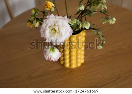 A bouquet of peonies in a yellow ceramic designer vase.In the kitchen interior . It's on the table .