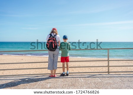 Mother with children standing by rail and relaxing looking at sea beach, sunshine outdoors background. Back view of recreation people dreaming romantic image