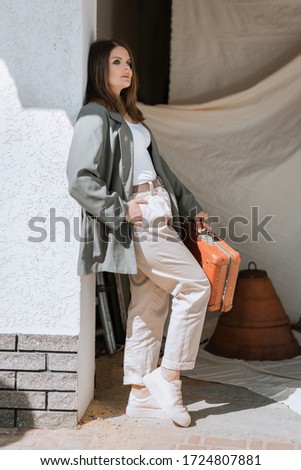 beautiful stylish girl, dressed in a loose jacket and pants, sits in a garage on a background of fabric