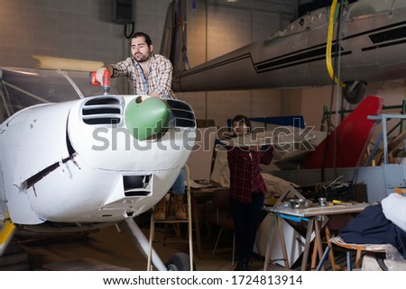 Young male aircraft enthusiast with female assistant working in workshop on creating of light aircraft flying model 