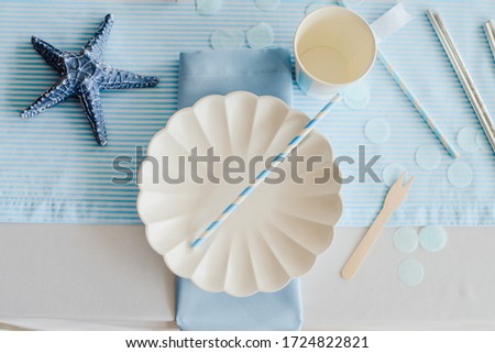 Tableware and decorations for serving festive table in sea style. Elegant plates, paper cups, straws with blue decorative textile. Birthday or baby shower boy .