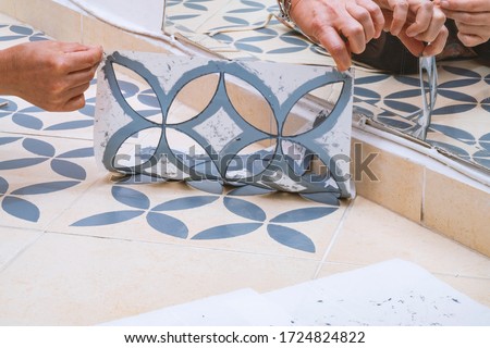 Stay at home and home improvement concept: Close up of hands removing a decorative painting stencil with a vintage design from the floor tiles after successfully painted into gray. Royalty-Free Stock Photo #1724824822