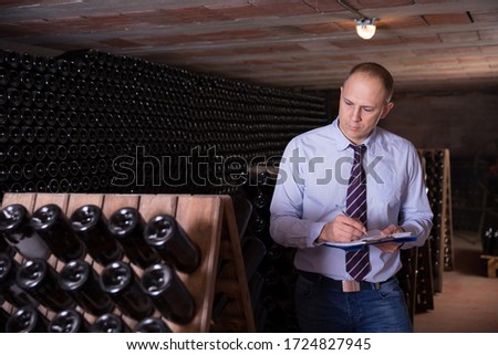 Winemaker controlling production wine in winery vault, noting in notebook
