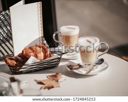 Still life of cups of cappuccino, croissants and maple leaf on a table in a classic French cafe in Paris in autumn