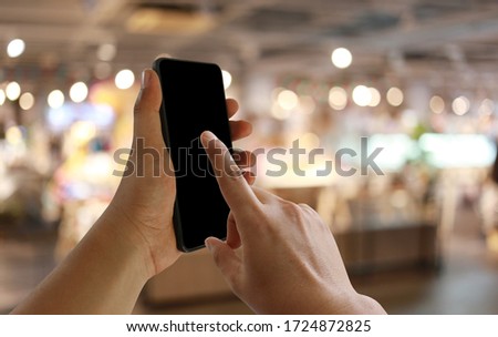 Hand of a businessman hold smartphone and use finger point to empty screen on restaurant and cafe background