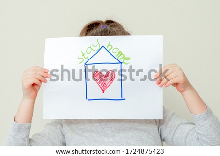 Closeup of child's hands holding a picture of red house with heart and words Stay Home covering her face. Stay Home concept.