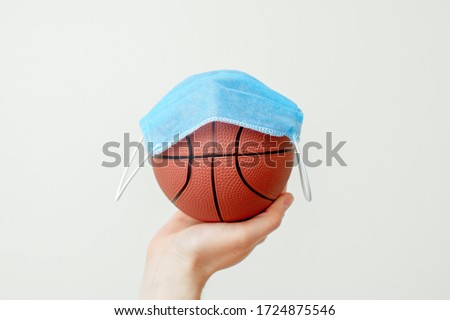 Protective medical mask over basketball ball on male hand due to the coronavirus epidemic on light background. Concept protection from viruses and infections.