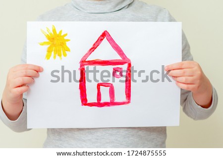 Closeup of child is holding picture of red house with sun at elementary school. Painting concept.