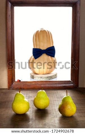 A pumpkin with a bow tie on an isolated background in an old frame and three ripe pears in the foreground