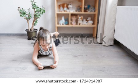 Distance learning. Little girl lying on a wooden floor with a phone, watching a cartoon or making a video call on a computer