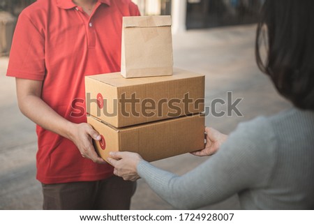 Deliver man wearing face mask in red uniform handling yellow bag of food, fruit, milk, vegetable give to female costumer Postman and express grocery delivery service during covid19. Royalty-Free Stock Photo #1724928007