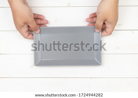 Empty square plate in the hands with copy space. Food concept with flat lay view above white wooden background.
