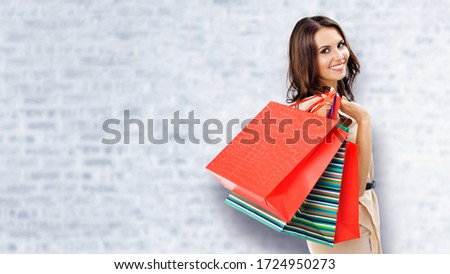 Shopping woman. Happy girl holding grocery bags, at white brick wall background. Copy space for some slogan, advertising or text. Brunette model - consumerism, sales and shopaholic concept picture. 