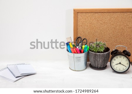 Copy space. Workplace office worker. Alarm clock, succulent in ceramic pot, writing board, bucket with scissors, felt-tip pens, ruler, three notebooks on student's desk.
