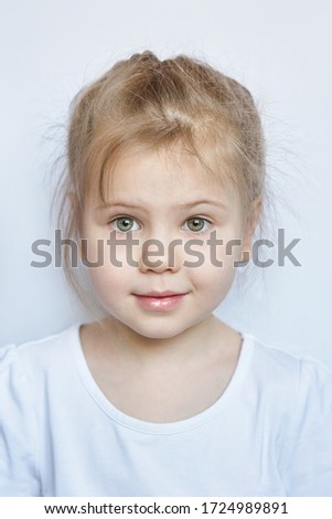 Portrait of a cute little Caucasian girl child with disheveled hair in a white t shirt on a light background