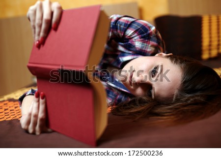 Young caucasian woman with long hair and plaid shirt reading a book on the bed, with selective focus