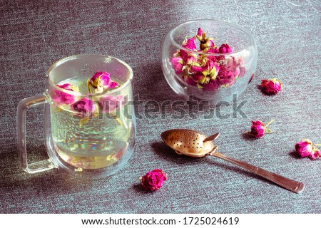 Glass transparent Cup with double walls and small roses in it. Exotic teas and drinks, karkade. Next to it is a tea spoon. Toned.Tea EvaDia Mei Gui Hua Bao, Rose buds close-up. Royalty-Free Stock Photo #1725024619