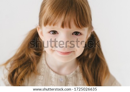 Portrait of a little red-haired girl on the stairs with freckles. Happiness, joy and a smile for children. Small model.