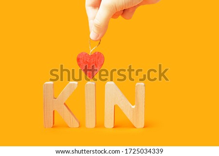 Word kin on orange background. Family concept. Hand holds heart over the word kin Royalty-Free Stock Photo #1725034339