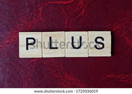  text the word plus from gray wooden small letters with black font on an red background