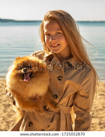 Portrait of beautiful red-haired girl 10 years old smile on a sandy beach near water with wonderful Pomeranian. photo content for Spitz kennels, veterinarians, dogs in social networks, blogs, websites