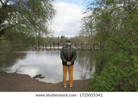 Lonely old man stands on the shore in the corona crisis and looks at a lake. Royalty-Free Stock Photo #1725055342