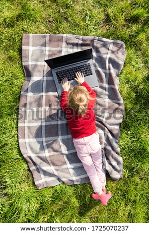 Child girl playing on a laptop in the garden. Online or Remote education concept. Top or aerial view.