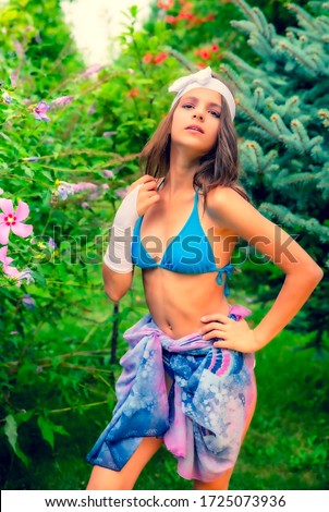 Model looking Girl standing in a swimsuit on the background of green grass and forest.