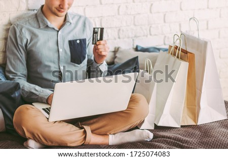 Closeup young happy man sit on couch, using laptop for safe online shopping from home. Stylish male hipster shopper hold credit card in hand. Payments and purchases at internet store. Man shopaholic Royalty-Free Stock Photo #1725074083