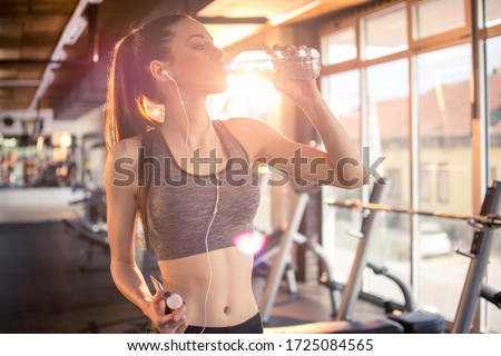 Portrait of beautiful young fit woman drinking water during traning in the gym. Royalty-Free Stock Photo #1725084565