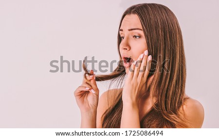 Portrait of frustrated surprised girl looking at her dry split ended hair tips isolated on background. Young sad worried woman holding long damaged unhealthy hair in hand. Hair loss problem treatment Royalty-Free Stock Photo #1725086494